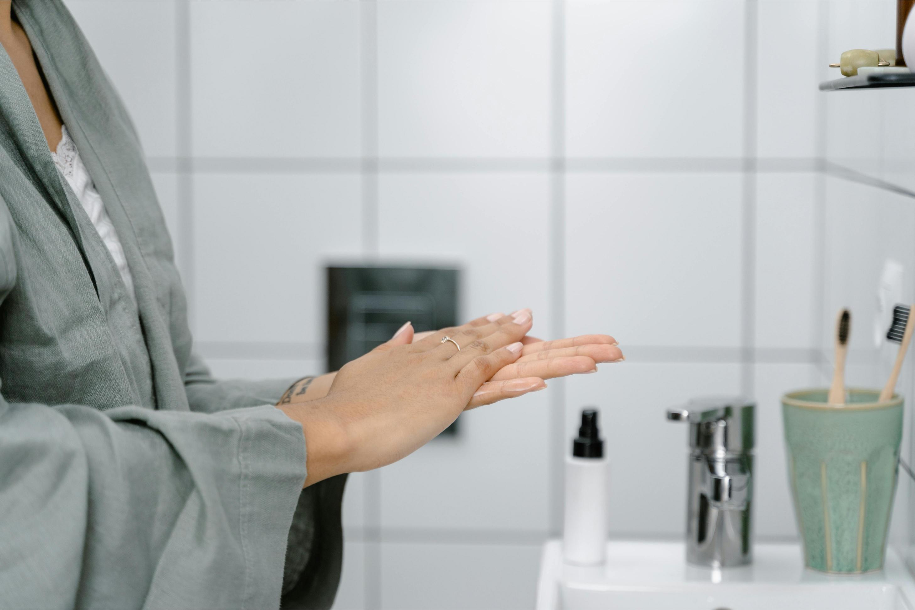 Woman in a bathroom in a robe rubbing skincare together in her hands above a bathroom sink