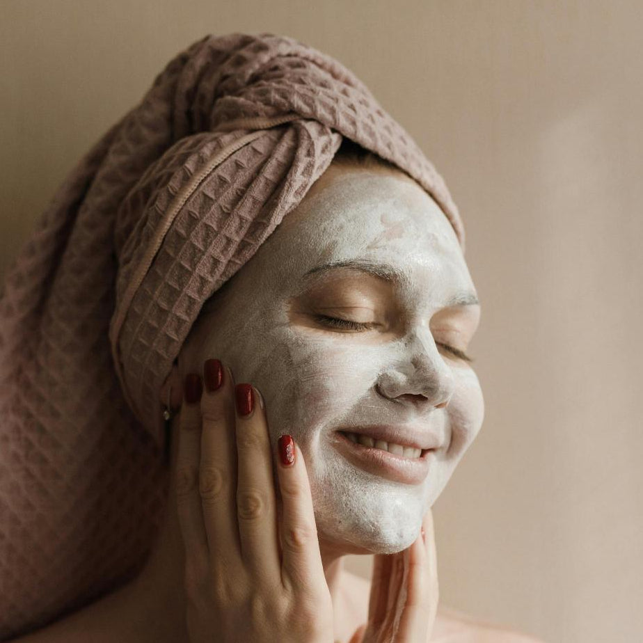 Woman with a facial mask and towel on her head, smiling.